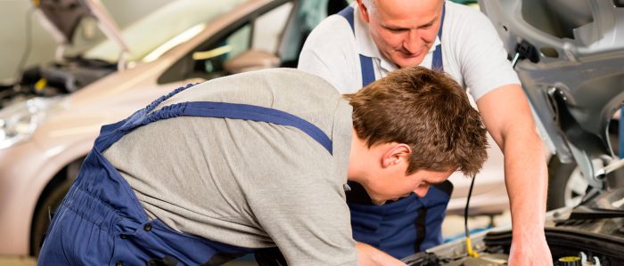 Meister zeigt seinem Azubi ein Teil in einem Automotor