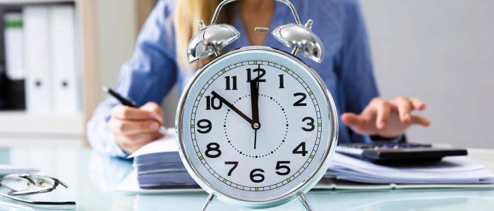 The picture shows a huge clock and a person working at a desk in the background.