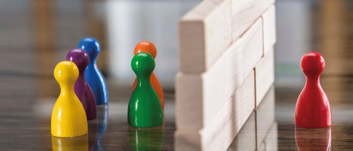 Sechs Spielfiguren, davon ist eine durch eine Mauer von den anderen getrennt