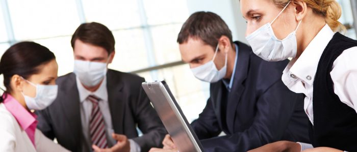 Gruppe von Beschäftigten, die um einen Arbeitstisch herumsitzen und Mundschutz tragen