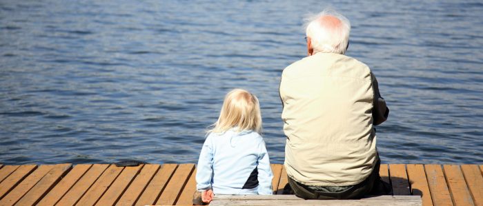 Opa und Enkelkind sitzen auf einem Steg und schauen aufs Wasser