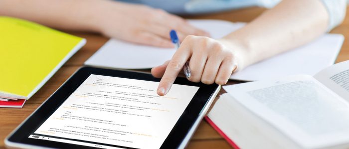 Bücher und Tablet auf einem Schreibtisch, an dem eine junge Frau sitzt