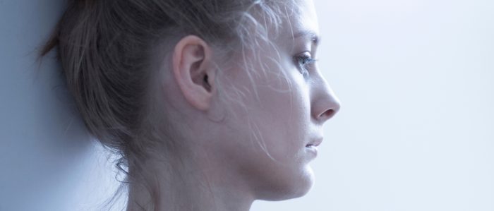 Traurige Frau hat den Kopf gegen die Wand gelehnt lehnt und starrt mit leerem Blick geradeaus