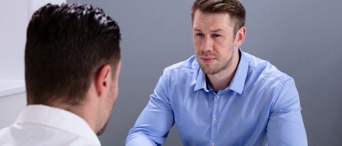 Zwei Männer sitzen sich an einem Tisch gegenüber. Einer der Männer hört dem anderen aufmerksam zu.