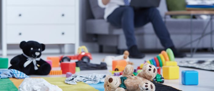 Mann sitzt mit Laptop auf der Couch, auf dem Boden liegt Kinderspielzeug