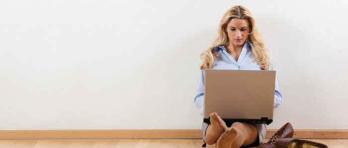 Junge Frau sitzt mit Laptop auf dem Fußboden
