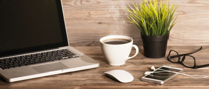 Schreibtisch mit Laptop, Kaffeetasse, Smartphone, Brille und Tischpflanze