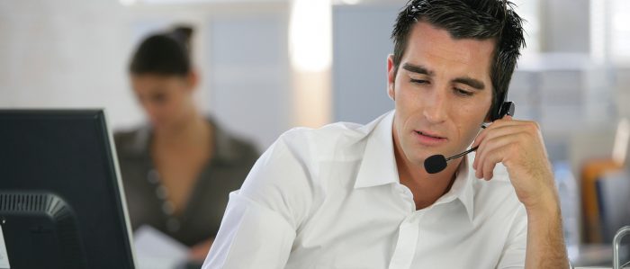 Männlicher Mitarbeiter sitzt am Arbeitsplatz und spricht in das Mikrofon seines Headsets