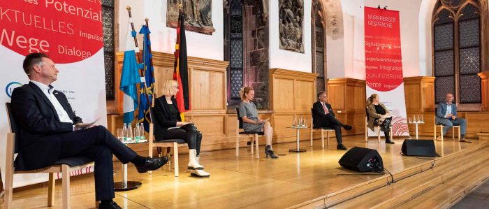 Podiumsgäste und die Moderatorin sitzen auf der Bühne der Nürnberger Gespräche in weitem Abstand auf Stühlen nebeneinander.