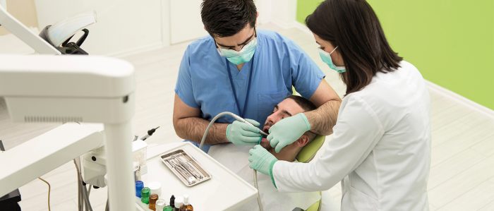 Zahnarzt mit Helferin, die beide Mundschutz und Handschuhe tragen, behandeln einen Patienten