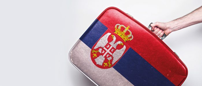 Eine Hand trägt einen Koffer in den serbischen Nationalfarben.