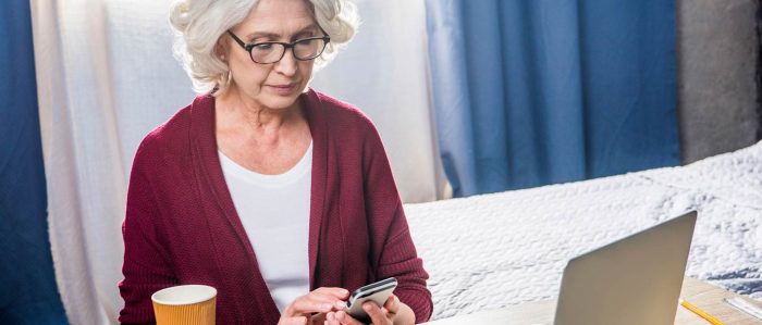 Frau sitzt zu Hause am Laptop und bedient ihr Smartphone