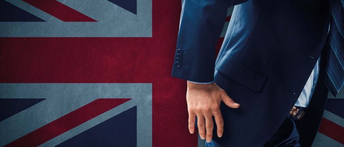 Mann im Anzug vor einer britischen Flagge, der gerade im Begriff ist, schnell wegzugehen