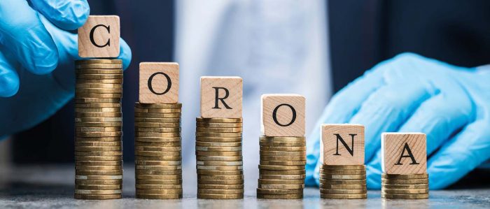 Sechs unterschiedlich hohe Türme aus Münzen mit jeweils einem Scrabblebuchstaben an der Spitze, die zusammen das Wort Corona ergeben.