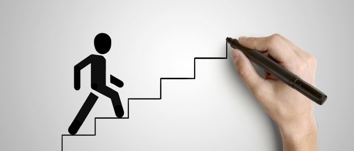 Menschliche Hand zeichnet mit einem Stift eine Treppe, die von einem Strichmännchen bestiegen wird.