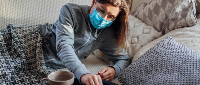 Frau mit Mundschutzmaske liegt zu Hause auf der Couch