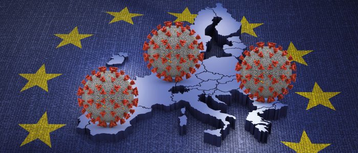 Three coronavirus balls are rolling over a map of the European continent. In the background stars of the European Union flag are shown.