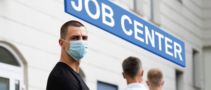 Mehrere Männer mit Mundschutzmaske stehen vor einem Jobcenter