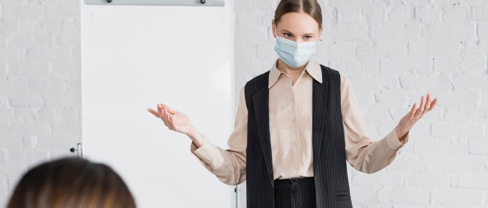 Frau mit Maske steht an einem Flipchart und erklärt etwas