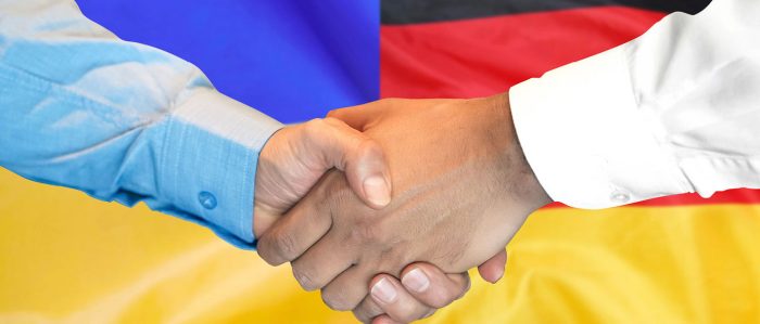 Zwei Männer geben sich vor einer deutschen und ukrainischen Flagge die Hand.