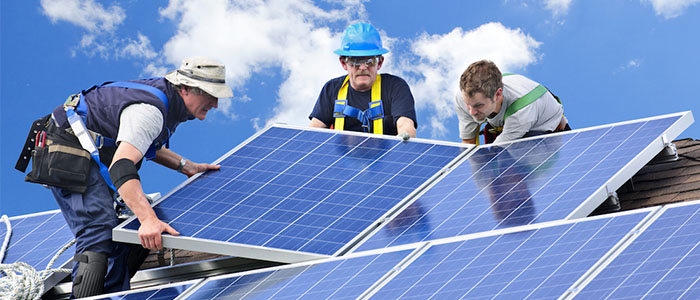Drei Arbeiter installieren Photovoltaik-Elemente auf einem Dach