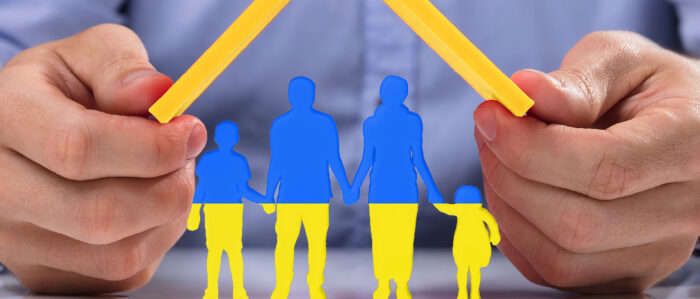 One hand holds a stylized roof over drawn people who have the color of the Ukrainian flag.
