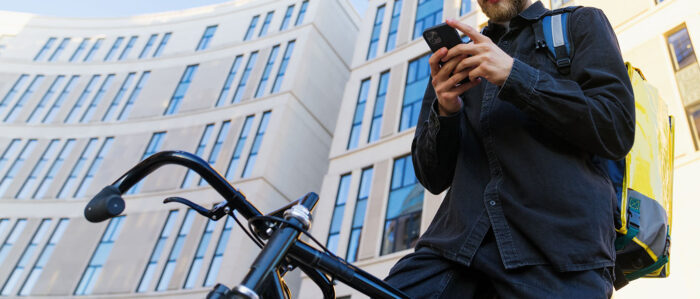 Ein männlicher Fahrradkurier überprüft in der App auf seinem Handy die neue Bestellung.