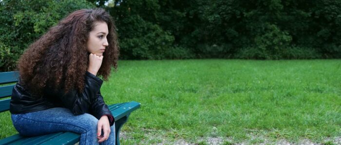 Ein ernst blickendes junges Mädchen sitzt im Park auf einer Bank.